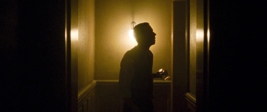 Silhouette d'Albert de profil dans un couloir sombre éclairé d'une lanterne