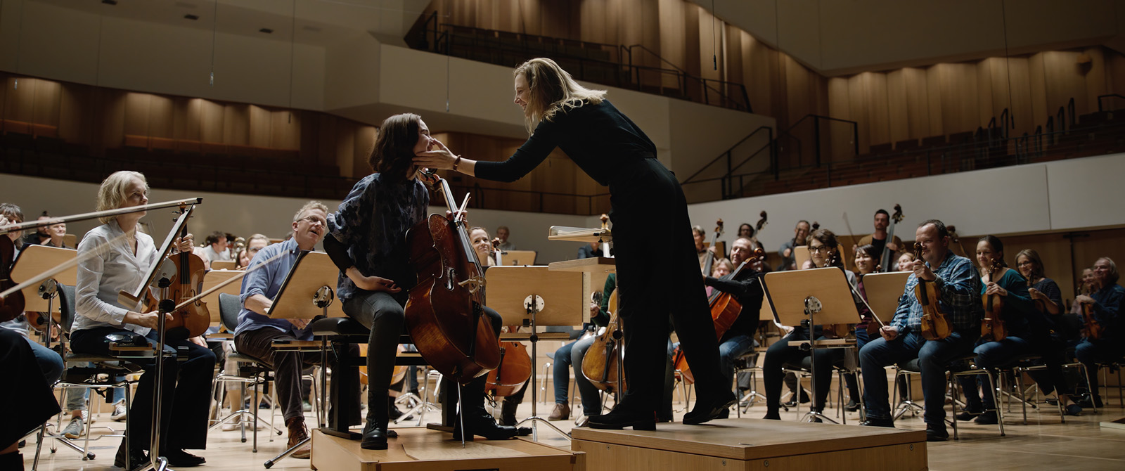cheffe d'orchestre (Lydia) caressant la joue d'une violoncelliste de l'orchestre symphonique de Berlin