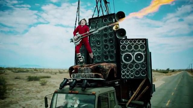 Attaché sur le capot d'un camion, Conan O'Brien joue de la guitare électrique pendant qu'Andy Ritcher conduit, déguisé en Immortan Joe !